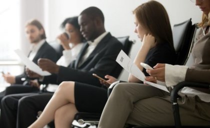 A line of people in suits sitting in chairs holding pieces of paper